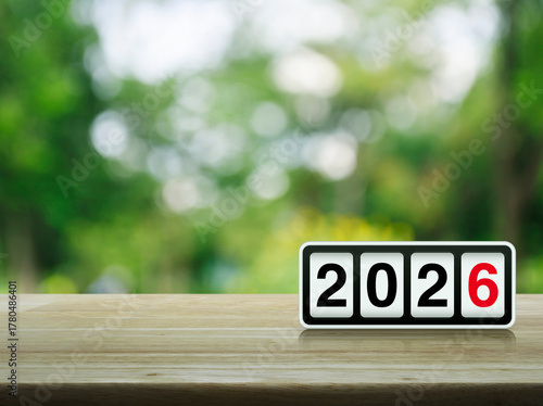 Retro flip clock with 2026 text on wooden table over blur green tree in park, Happy new year 2026 cover concept