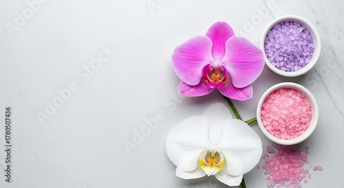 Close-up shot of vibrant pink and white orchids with bowls of colorful bath salts on a marble surface.