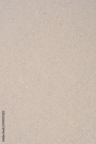 A close-up of light brown-gray recycled cardboard or heavy paper featuring a rough, uneven texture and visible small dark fiber flecks