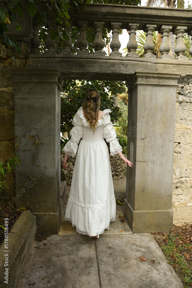 Obraz premium Full length female figure of beautiful blonde model wearing white fantasy wedding gown. walking through doorway of historical fairytale castle location