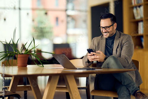 Professional Man in Blazer Uses Phone at Modern Office With Laptop and Plant
