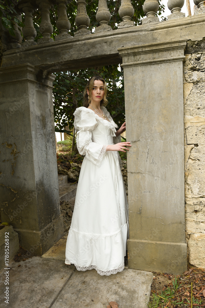 Fototapeta premium Full length female figure of beautiful blonde model wearing white fantasy wedding gown. walking through doorway of historical fairytale castle location