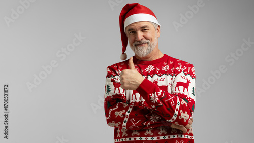 Merry satisfied smiling mature man wear knitted christmas sweater Santa hat showing thumb up. Happy New Year 2026