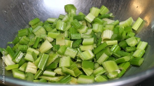 A gloved hand holds a kitchen knife mid-cut as crisp green celery is chopped into uniform pieces on a vibrant board, highlighting precision and food safety in preparation.