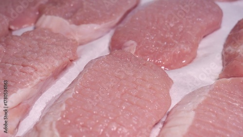 Fresh pork chops with visible marbling rest on a white surface, lightly dusted with black pepper, showcasing moisture, texture, and early seasoning in a kitchen setting