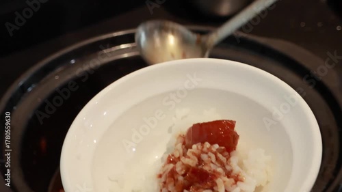 Stirring and pouring braised pork belly meat over cooked rice.