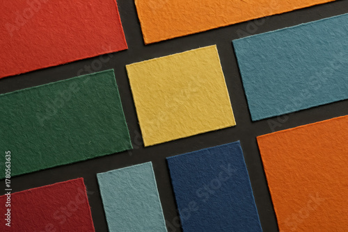 Colorful sheets of textured paper arranged in a grid for art and design projects in soft lighting