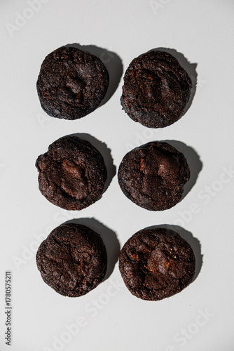 A neatly arranged set of six rich, dark chocolate cookies placed in a grid formation on a clean white surface. The cookies appear moist, dense, and fudgy, suggesting a deep cocoa flavor