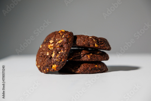 A stack of rich double chocolate cookies with nut chunks arranged on a white surface, showcasing texture and contrast. No visible branding