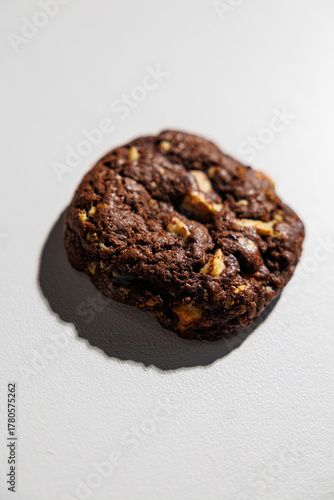 One rich, dark chocolate cookie with chunks of nuts sits centered on a white surface, highlighting its texture and contrast. No branding is visible