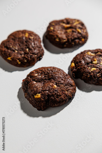 A flat lay of four dark chocolate cookies with visible nut chunks, arranged neatly on a white surface. No branding or packaging is visible