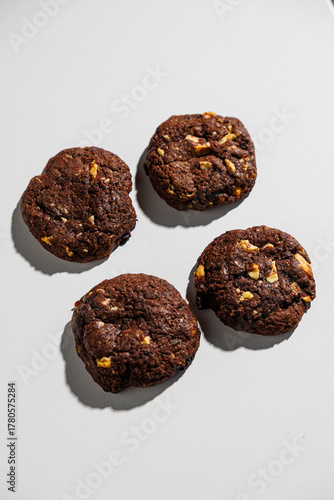 A flat lay of four dark chocolate cookies with visible nut chunks, arranged neatly on a white surface. No branding or packaging is visible