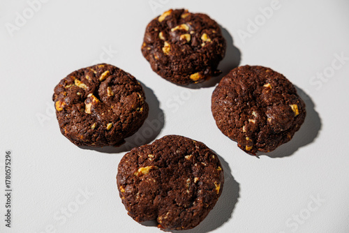 A flat lay of four dark chocolate cookies with visible nut chunks, arranged neatly on a white surface. No branding or packaging is visible