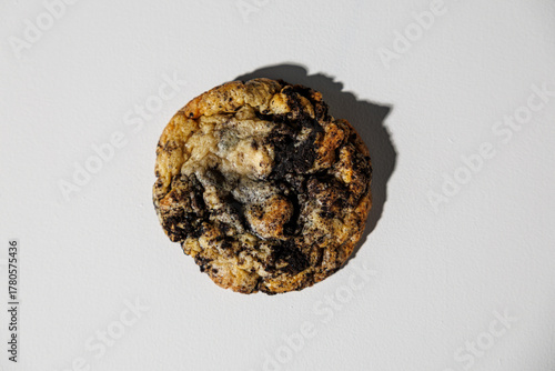 Close-up of a single golden cookie embedded with crushed chocolate sandwich cookie chunks, isolated on a white background. No visible branding