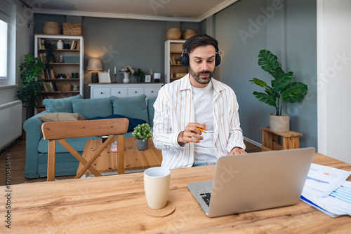 Foto Young freelancer leading an online video meeting from a cozy home office smiling man with headphones gestures while speaking on a laptop during remote consulting and sharing project results