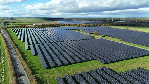 Aerial view of rows of dark solar panels contrast with the lush green fields under a sky of white clouds, creating a stark juxtaposition of energy and nature, Mansfield, England, United Kingdom.