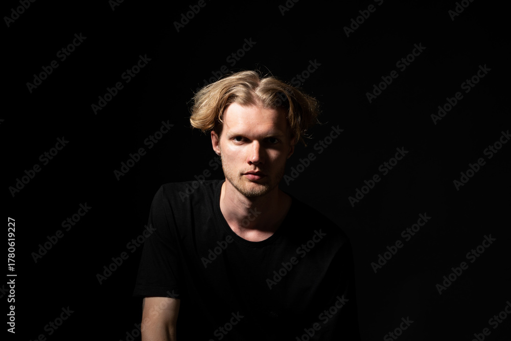 Fototapeta premium Confident man in black shirt looking forward in low key portrait with focused expression