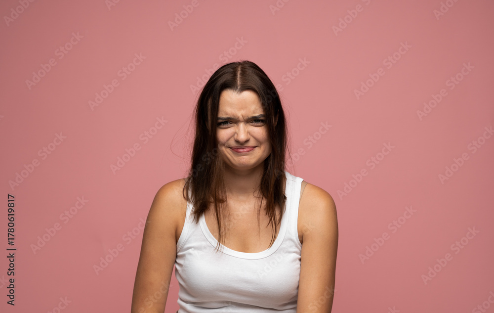 Obraz premium Studio portrait of young woman frowning with confused facial expression on pink background