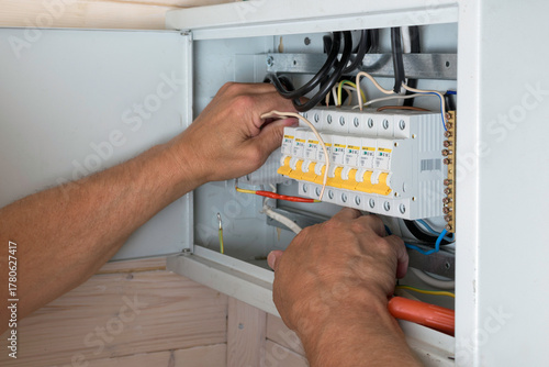Electrician's skilled hands install wires inside distribution board, ensuring reliable and safe electrical connection in new home.