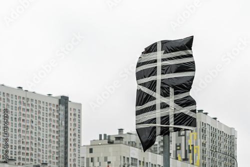 Traffic sign wrapped in black plastic and tape stands against city high-rise buildings, symbolizing urban transformation and adaptation.