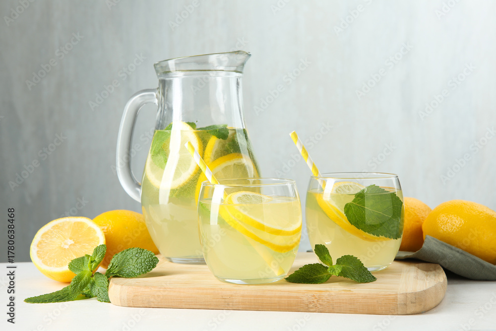 Fototapeta premium Fresh lemonade in glasses, jug, lemons and mint on white table