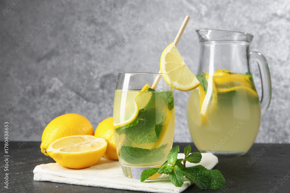 Fototapeta premium Fresh lemonade in glass, jug, lemons and mint on black table, closeup