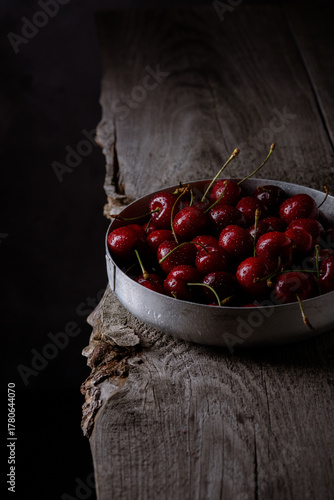 Ripe fresh cherries in an iron bowl on a wooden table. Dark background.