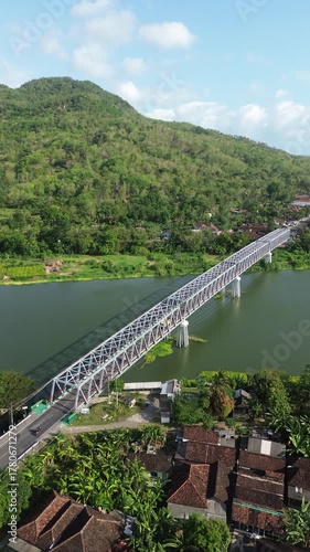 Long White Truss Bridge Spanning A Wide River Over Lush Hillside Valley Landscape