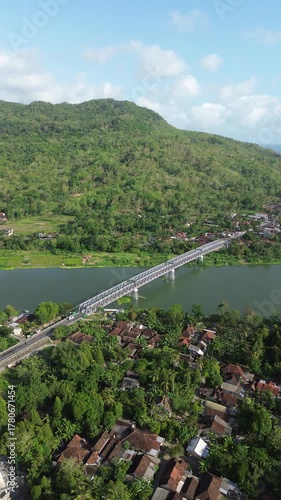 Long White Truss Bridge Spanning A Wide River Over Lush Hillside Valley Landscape