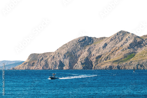Small boat navigating blue waters near rocky island coastline. Isolated object