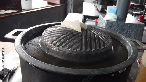 Traditional Thai barbecue grill pan, known as Moo Kratha, with a piece of pork lard melting on top. Popular Thai-style BBQ combining grilling and hotpot cooking in one pan.