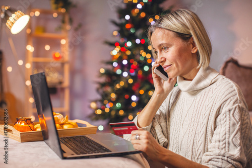Attractive Smiling middle aged lady with laptop sitting at home and buying xmas gifts