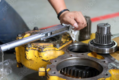 A mechanic using a torque wrench to tighten a bolt on a yellow heavy machinery transmission or differential casing during assembly and professional maintenance work.