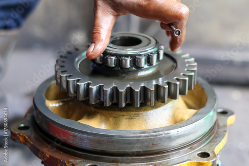 Close-up of a mechanic's hand installing a large planetary gear and a roller bearing assembly onto a yellow industrial machine housing during a precision repair.