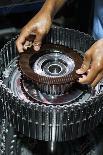 A technician's oily hands assembling a clutch friction plate onto the metallic hub of an automatic transmission clutch pack, detailing automotive repair work.
