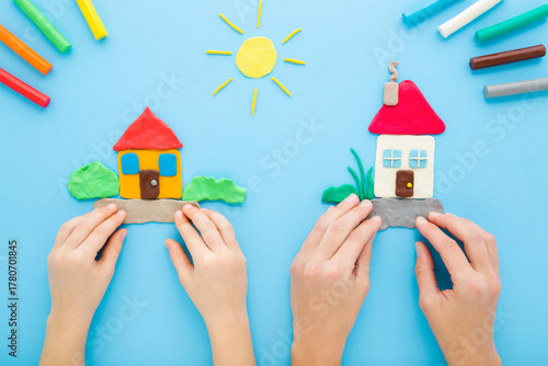 Young adult mother and little child hands together making and creating houses from colorful modeling clay on light blue table background. Pastel color. Closeup. Point of view shot. Top down view.