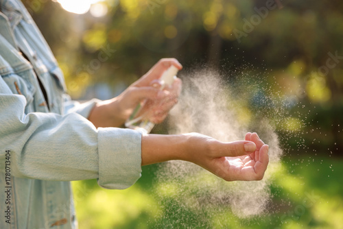Quadro em tela Woman spraying tick repellent onto hand in park, closeup