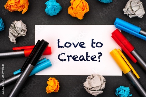 White paper blank with words Love to Create? with colour pens and crumpled paper balls around it on a black background.