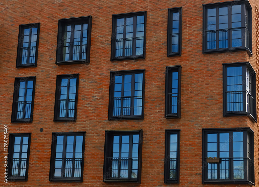 Fototapeta premium Exterior of modern brick house object. Architectural detail of a skyscraper, close-up on the windows. Real estate, residential apartments and offices. Living apartments or office building architecture