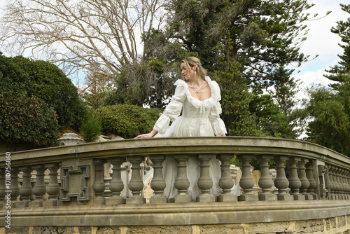portrait of beautiful young blonde model wearing fantasy white wedding ballgown. romantic figure posing on balcony of historical fairytale castle location 