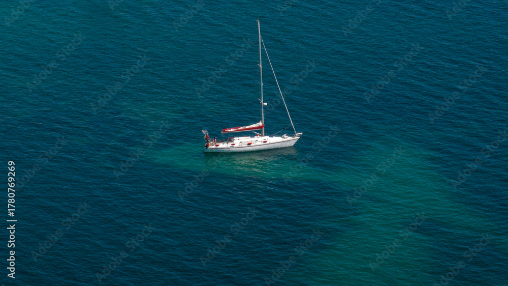 Fototapeta premium Aerial view of a white sailboat sailing in the blue and calm sea.
