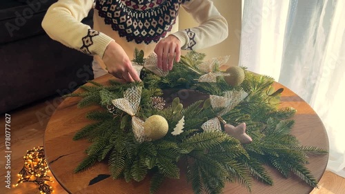 Woman hands in a Christmas sweater decorating a festive wreath with a candle, cozy holiday atmosphere at home, no face