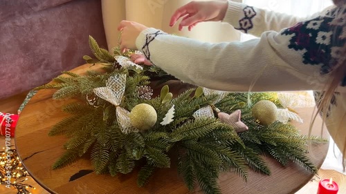 Woman in a Christmas sweater decorating a festive wreath with a candle, cozy holiday atmosphere at home