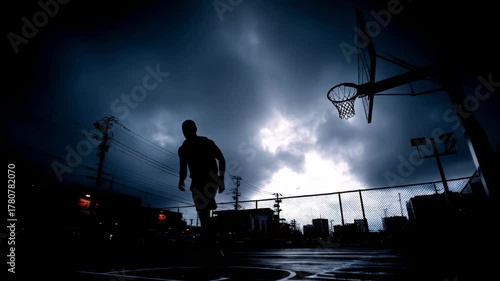 Silhouetted players dribble on a dim outdoor basketball court at dusk, under dramatic clouds nearby