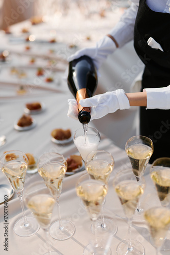 The waiter pours champagne into glasses before the celebration