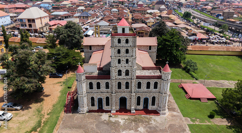 Aerial view of a magnificent church standing tall amidst lush greenery, its red rooftops contrasting with the earthy tones of the surrounding buildings, Ado, Ekiti, Nigeria.