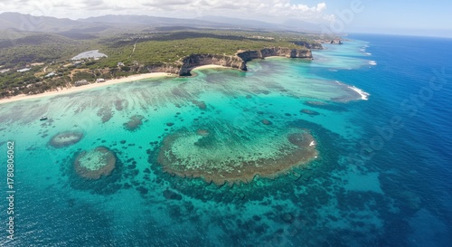 Aerial perspective captures vibrant turquoise ocean waters meeting lush coastal cliffs and sandy shorelines