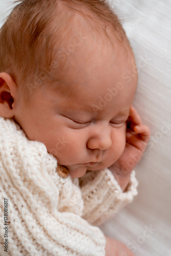 newborn baby sleeping on a white bed at home, close-up portrait of a newborn baby sleeping in a white knitted bodysuit, space for text