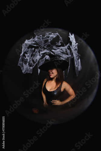 portrait of a young witch in hat on black background with spider net