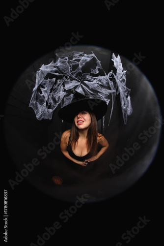 portrait of a young witch in hat on black background with spider net